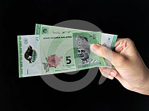 Hand holding a Bank Negara Malaysia 5 Ringgit Moneys over black background