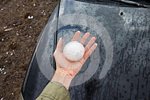 Hand holding a baseball sized hail stone dropped by a supercell thunderstorm.