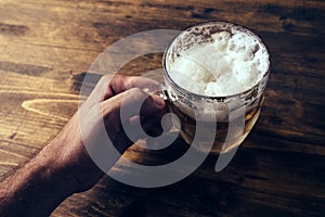 Hand holding beer mug full of cold fresh alcohol drink