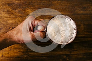 Hand holding beer mug full of cold fresh alcohol drink