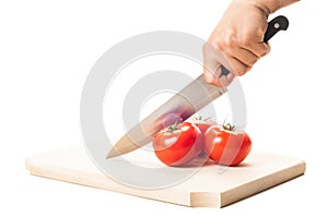 Hand holding a big knife, three tomatoes and wooden board