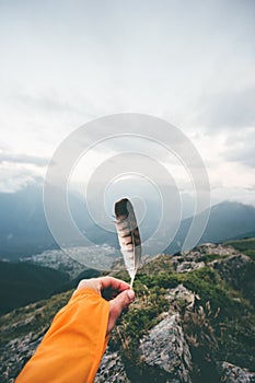 Hand holding bird feather moody mountains landscape