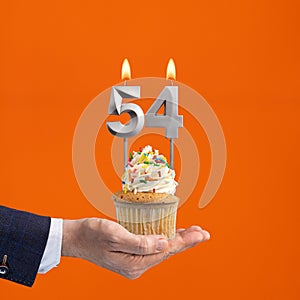 Hand holding birthday cupcake with number 54 candle - background orange
