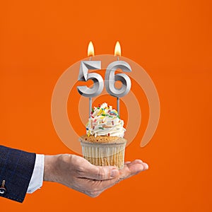 Hand holding birthday cupcake with number 56 candle - background orange
