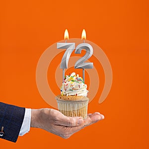 Hand holding birthday cupcake with number 72 candle - background orange