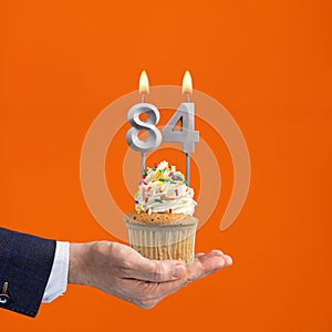 Hand holding birthday cupcake with number 84 candle - background orange