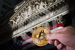 Hand holding a bitcoin and blurred NYSE in the background