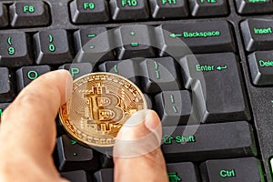 Hand holding bitcoin lying on computer keyboard