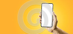 Hand holding black cellphone with blank screen and modern frame less design on yellow background. smartphone showing white blank