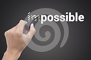 Hand holding black eraser changing the word impossible