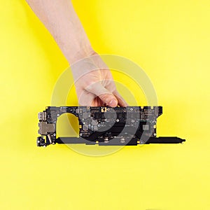 Hand holding black laptop pcb main board repair on yellow background top view