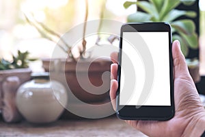 A hand holding black mobile phone with blank white desktop screen on vintage wooden table in cafe