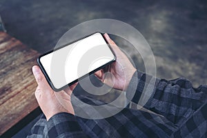 Hand holding black mobile phone with blank white screen horizontally in vintage cafe