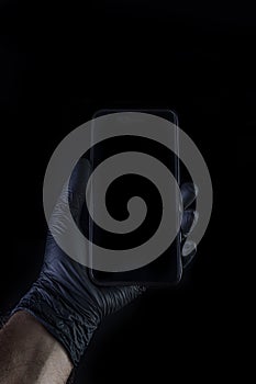 Hand holding a black phone isolated on a black background with a black gloves.