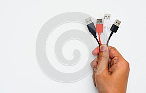 Hand holding black, red and white color USB cables on white wall background, copy space