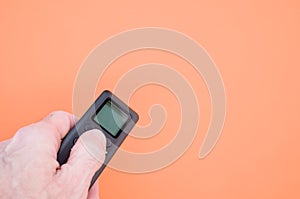 Hand holding a black remote controller on an orange background