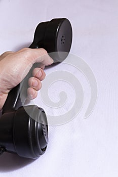 Hand holding black telephone horn to make call to the past. White cloth background with antique telephone in hand.