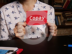 Hand holding a blank piece of paper with inscription Copay . Close up white business card