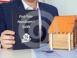 Hand holding a blank piece of paper with inscription First-Time Homebuyer`s Guide . Close up white book