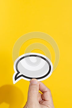 Hand holding a blank speech bubble isolated on yellow background