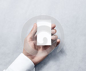 Hand holding blank vertical white business card design mockup.