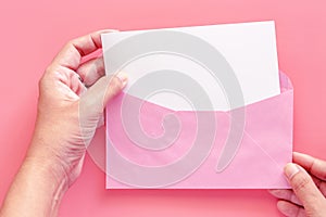 Hand holding blank white greeting paper card in pink envelope