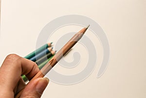 A hand holding a blending pencil for colored pencils with several colored pencils in the background