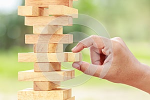 Hand holding blocks wood game (jenga) on blurred green background. Risk concept photo