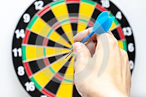 A hand holding a blue dart ready to throw it to a dartboard target, strategy and skill in business concept