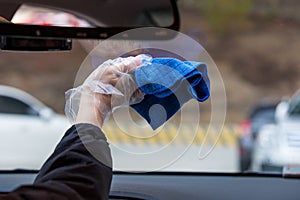 Hand holding a blue fiber towel to wipe the car window. Cleaning car`s windshield with microfiber cloth