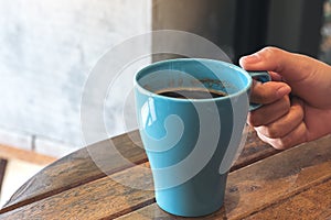 A hand holding blue mug of hot coffee on vintage wooden table in cafe