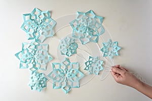 Hand holding blue paper snowflakes balloons with threads laying on white background. Top view. Christmas decoration