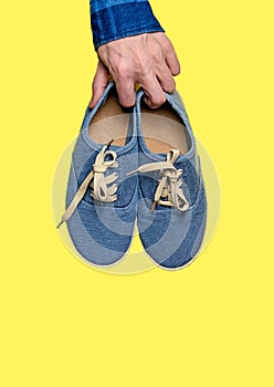 Hand holding blue sneakers  on a yellow background. Sports shoes hanging.