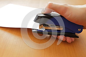Hand holding blue stapler stapling papers photo