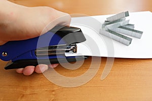 Hand holding blue stapler stapling papers