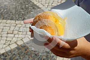 Hand holding Bola de Berlim or Berlim Ball, a Portuguese pastry made from a fried donut filled with sweet eggy cream and photo