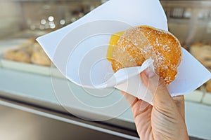 Hand holding Bola de Berlim or Berlim Ball, a Portuguese pastry made from a fried donut filled with sweet eggy cream and photo