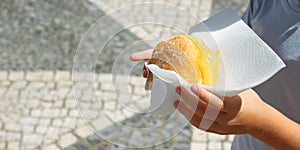 Hand holding Bola de Berlim or Berlim Ball, a Portuguese pastry made from a fried donut filled with sweet eggy cream and photo