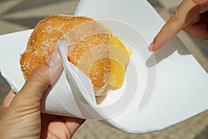 Hand holding Bola de Berlim or Berlim Ball, a Portuguese pastry made from a fried donut filled with sweet eggy cream and photo
