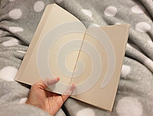 Hand holding a book on a warm fleece blanket