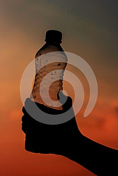 Hand holding bottle water on sunset sky,Summer holiday vacation outdoor and view in evening,