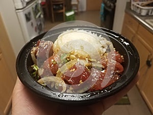 Hand holding bowl of raw tuna and onions and rice