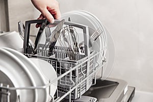 Hand holding box with clean cutlery in open dishwasher in the home kitchen