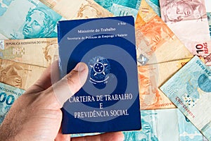 Hand holding Brazilian document work and social security Carteira de Trabalho e Previdencia Social with Brazilian money