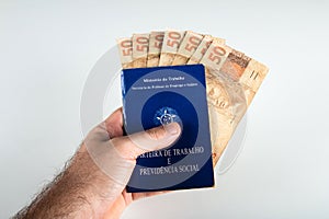 Hand holding Brazilian document work and social security Carteira de Trabalho e Previdencia Social with fifty reais banknotes.