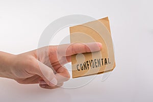 Hand holding a brown color paper with text confidental