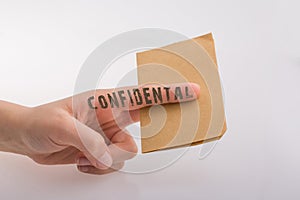 Hand holding a brown color paper with text confidental