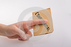 Hand holding a brown color paper with text confidental