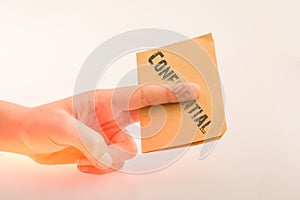 Hand holding a brown color paper with text confidental