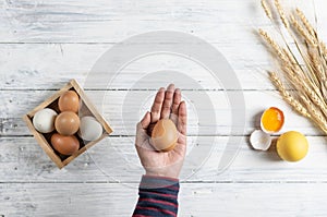 Hand holding brown egg on white wood background